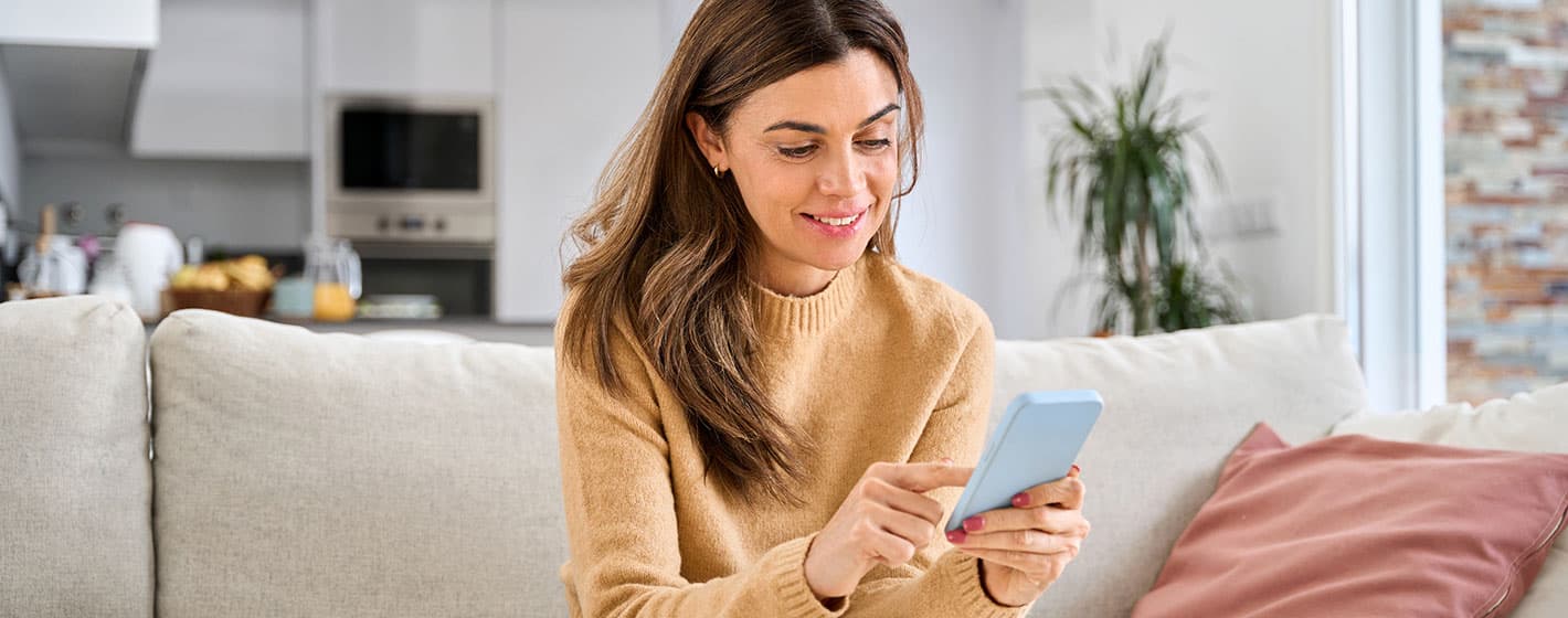 Bild: Frau sitzt auf Sofa mit Handy in der Hand.
